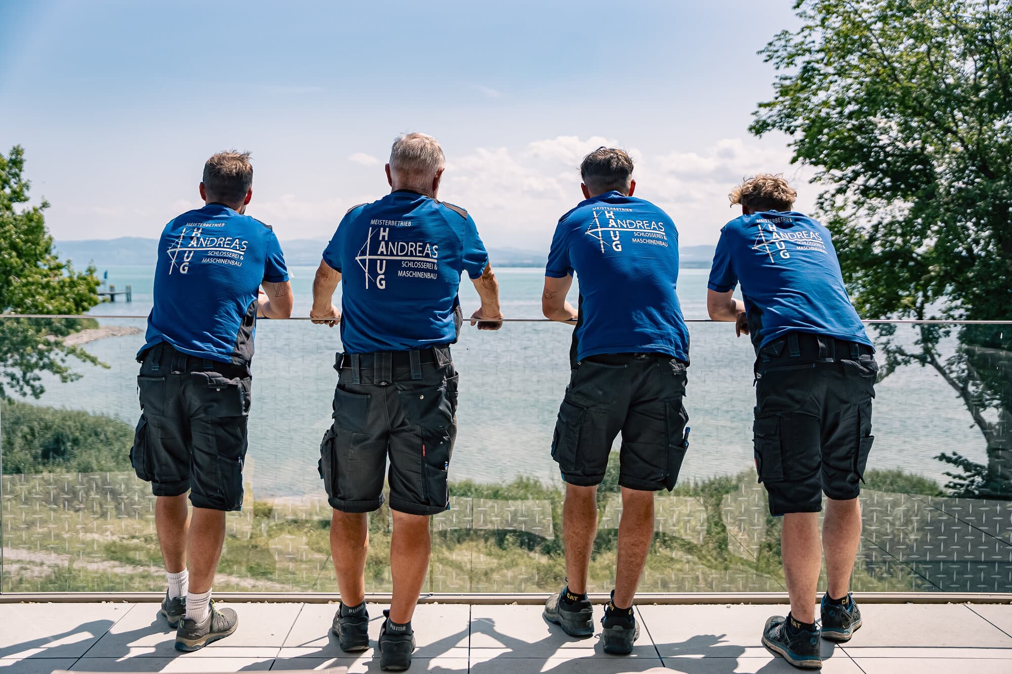 Vier Mitarbeiter der Haug GmbH an einem selbst gebauten Glasgeländer mit Blick auf den Bodensee